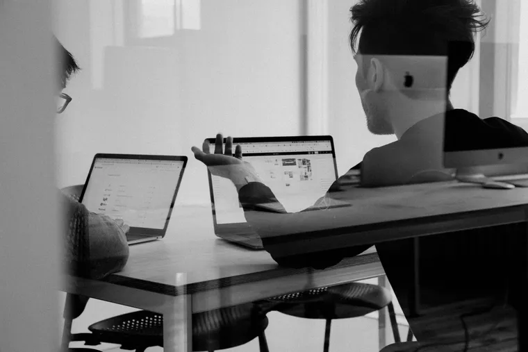 Two people working side by side on laptops at a shared desk