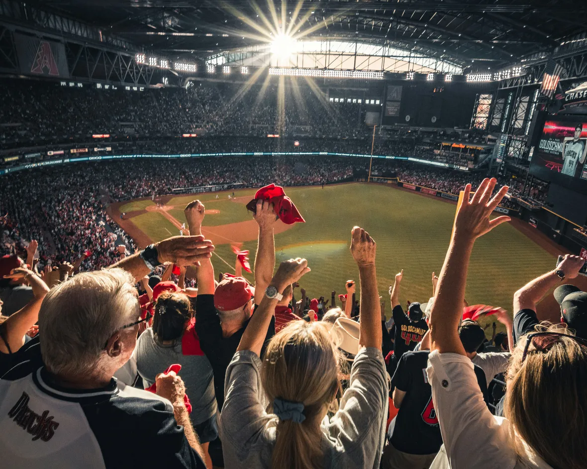 A packed stadium crowd cheering with raised arms